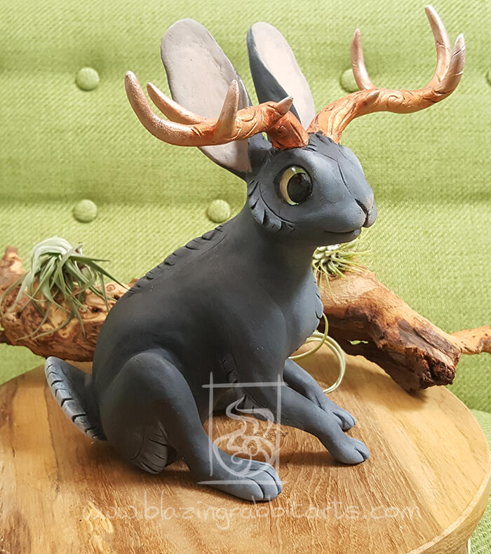 Sculpture of a black Jackalope with copper horns sitting.